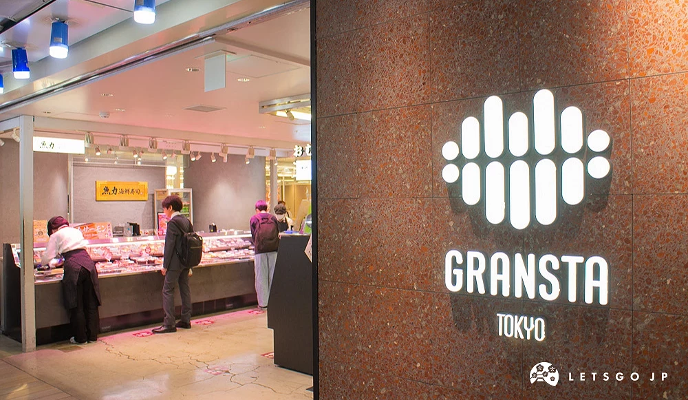 GRANSTA TOKYO 標誌亮起白光並鑲嵌於紅棕色石牆,背景為商場內部的生鮮櫃檯。